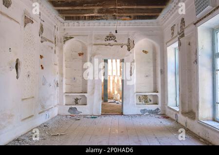 Blick auf ein verlassenes Bauwerk, das jetzt größtenteils ruiniert ist und auf die Restaurierung wartet. Ein schlichtes, weiß getünchtes Nebenzimmer. In einem alten, historischen, klassischen, traditionellen Stockfoto