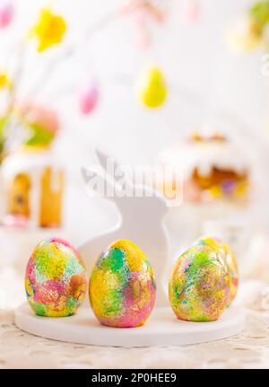 Osterkomposition mit bunten Ostereiern auf Kaninchen-Dessertplatte. Traditionelles Ostergeschenk auf festlichem Tisch, dekoriert mit Frühlingsblumen. Stockfoto