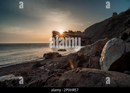 Ein epischer Sonnenuntergang auf dem Meer - die Sonne geht hinter dem Berg unter und alles scheint mit warmem Licht und langen Strahlen. Stockfoto