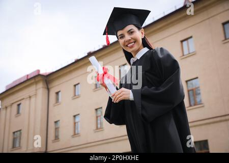 Glücklicher Student mit Abschluss nach der Abschlussfeier im Freien, Blick aus dem niedrigen Winkel. Platz für Text Stockfoto