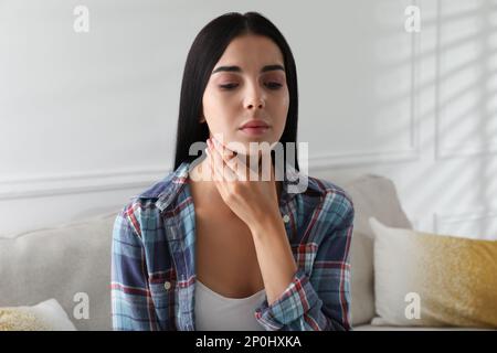 Junge Frau, die zu Hause eine Schilddrüsen-Selbstuntersuchung macht Stockfoto