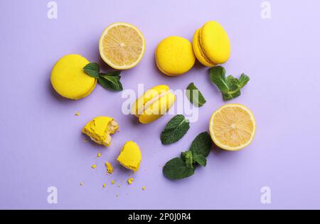 Flache Laienzusammensetzung mit gelben Makronen, Minze und Zitrone auf violettem Hintergrund Stockfoto