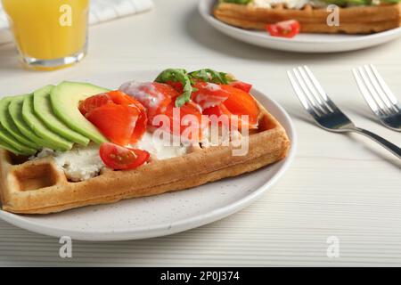 Köstliche belgische Waffeln mit Lachs, Avocado und Rucola auf einem weißen Holztisch Stockfoto