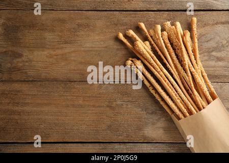 Köstliche Grissini-Sticks in Papiertüte auf Holztisch, Draufsicht. Platz für Text Stockfoto