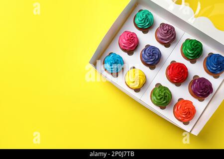 Box mit verschiedenen Cupcakes auf gelbem Hintergrund, Draufsicht. Platz für Text Stockfoto