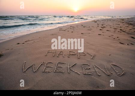 Text Happy Weekend geschrieben am Sandstrand bei Sonnenuntergang Stockfoto