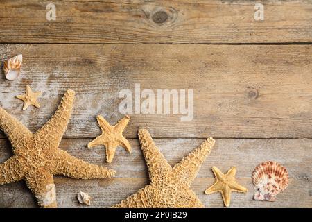 Wunderschöne Seesterne, Muscheln und Sand auf Holzhintergrund, flach liegend. Platz für Text Stockfoto