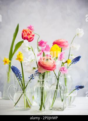 Wunderschöne Blumensträuße in Glasvasen auf dem Holztisch. Tulpen, Rosen, Muscari, Narzisse, Eustoma und Hyazinthen Stockfoto