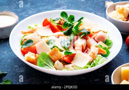 Caesar Salat mit Garnelen, Eisbergsalat, Croutons, Parmesan und Tomaten mit caesar Dressing. Blauer Tabellenhintergrund, Draufsicht Stockfoto