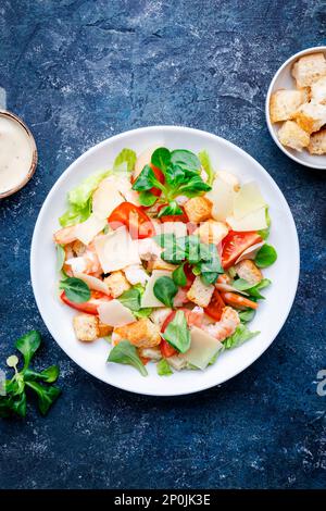 Caesar Salat mit Garnelen, Eisbergsalat, Croutons, Parmesan und Tomaten mit caesar Dressing. Blauer Tabellenhintergrund, Draufsicht Stockfoto