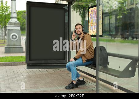 Junger Mann, der Musik hörte, während er an der Bushaltestelle auf öffentliche Verkehrsmittel wartete Stockfoto