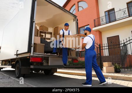 Arbeiter, die Kisten aus dem Lieferwagen im Freien entladen. Umzugsdienst Stockfoto