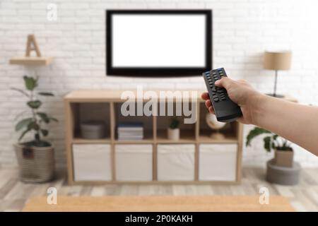 Ein junger Mann, der zu Hause mit Fernbedienung die Sender umschaltet, Nahaufnahme Stockfoto