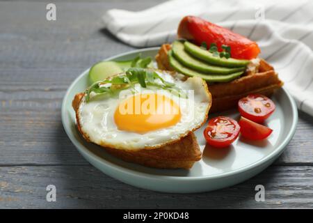 Köstliche belgische Waffeln mit Spiegelei, Rucola und Gemüse auf grauem Holztisch, Nahaufnahme Stockfoto