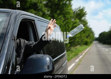 Der Fahrer wirft die Plastikflasche vom Autofenster weg. Müll auf der Straße Stockfoto