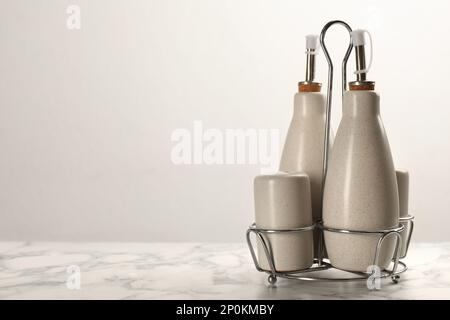 Sauceflaschen mit Salz- und Pfefferschüttlern im Halter auf dem weißen Marmortisch. Platz für Text Stockfoto