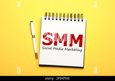 Notizbuch mit Text SMM (Social Media Marketing) und Stift auf gelbem Hintergrund, flach liegend Stockfoto