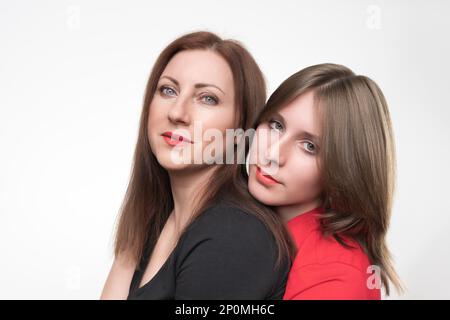 Porträt einer Frau, Mutter und Tochter, die in die Kamera schaut. Mom in schwarzem T-Shirt und Teenager in rotem T-Shirt. Studioaufnahmen auf weißem Hintergrund Stockfoto