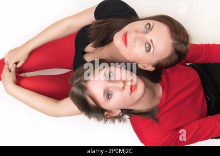 Draufsicht auf mutter und Tochter, die mit dem Rücken aneinander sitzen und sich die Köpfe auf die Schultern legen. Beide Frauen schauen vor die Kamera Stockfoto