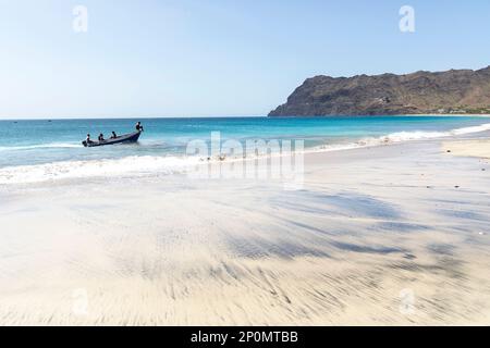 Fischer, die in einem hölzernen, bunten Boot in der Nähe eines Sandstrandes in einem Dorf Sao Pedro auf der Insel Sao Vicente, Cabo verde, fahren Stockfoto