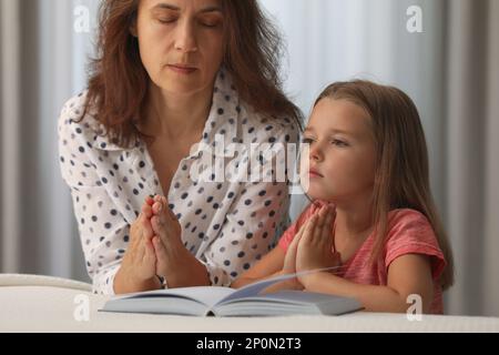 Reife Frau mit ihrer kleinen Enkelin betet zusammen für die Bibel im Schlafzimmer Stockfoto