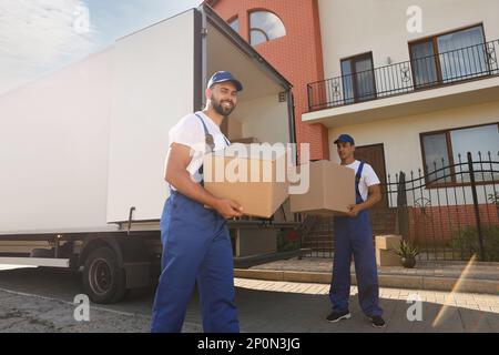 Arbeiter, die Kisten aus dem Lieferwagen im Freien entladen. Umzugsdienst Stockfoto