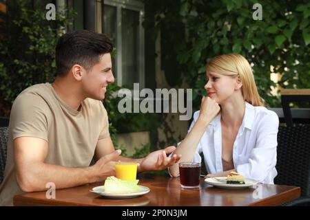 Junge Frau hat ein langweiliges Date mit einem gesprächigen Mann im Café draußen Stockfoto