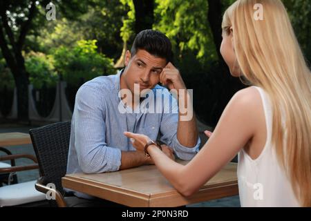 Ein Mann hat ein langweiliges Date mit einer gesprächigen Frau im Café draußen Stockfoto