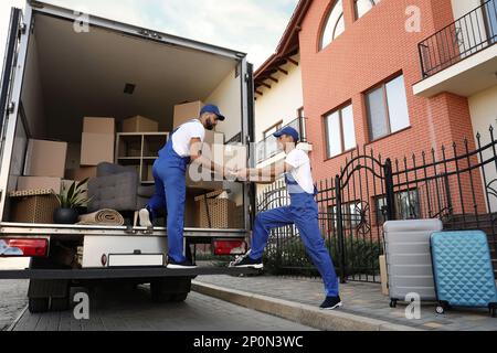 Arbeiter, die Kisten aus dem Lieferwagen im Freien entladen. Umzugsdienst Stockfoto