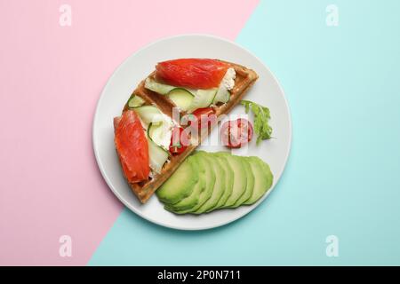 Köstliche belgische Waffeln mit Lachs, Avocado, Frischkäse und Gemüse auf farbigem Hintergrund, Draufsicht Stockfoto