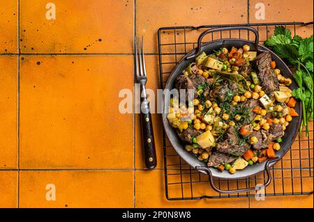 Spanischer Cocido Madrid Eintopf mit Kichererbsen, Fleisch, Karotten und Kartoffeln. Orangefarbener Hintergrund. Draufsicht. Speicherplatz kopieren. Stockfoto