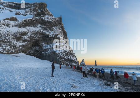 Reynisfjara Strand komplett mit Schnee bedeckt und die Basaltformationen beleuchtet von den letzten Sonnenstrahlen vom Horizont des Meeres mit Touri Stockfoto