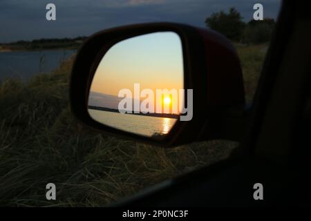 Reflexion der Landschaft mit wunderschönem Sonnenuntergang über dem ruhigen Fluss im Auto, Seitenspiegel, Nahaufnahme Stockfoto