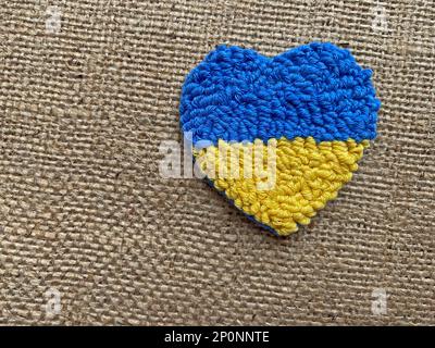 Stand mit ukrainischem Hintergrund: Herz mit ukrainischer Flagge auf brauner Leinwand Stockfoto