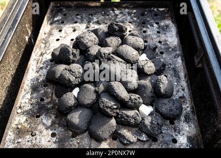 Beleuchten Sie einen Heimgrill mit Holzkohle und weißem Kamin für den Grill, der im Heimgarten steht. Stockfoto