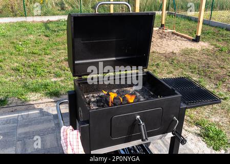 Beleuchten Sie einen Heimgrill mit Holzkohle und weißem Kamin für den Grill, stehen Sie im Heimgarten, und verwenden Sie einen Grillanzünder. Stockfoto