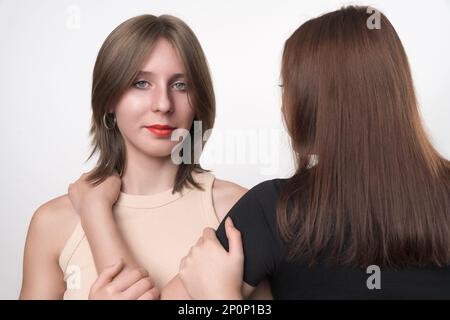 Porträt einer Tochter mit grauen Augen und langen Haaren, die vor der Kamera steht, die Mutter steht mit dem Rücken. Zwei Generationen, Teenager-Tochter Stockfoto