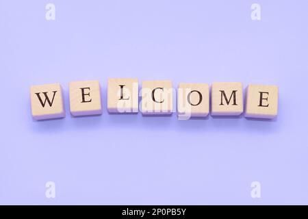 DAS Wort WELCOME besteht aus Holzwürfeln auf violettem Hintergrund. Stockfoto