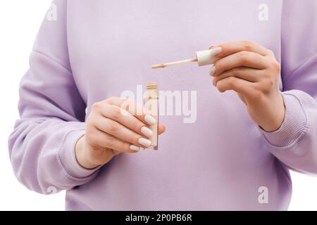 Nahaufnahme einer Frau in einem übergroßen Lavander-Sweatshirt mit einer Verdeckflasche und einer Bürste in den Händen. Schön gepflegte Nägel mit Nagellack. Stockfoto