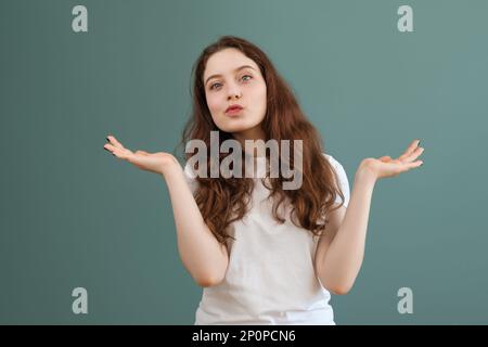 Ein braunes Teenager-Mädchen im weißen T-Shirt spreizt ihre Hände, auf blauem Hintergrund. Ich weiß nicht, verwirrte Geste. Stockfoto