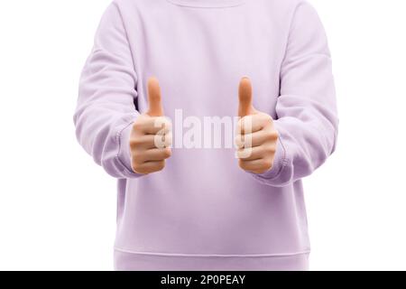 Die gekürzte Aufnahme einer Frau in einem übergroßen, lavendelfarbenen Sweatshirt zeigt zwei Daumen nach oben, wie ein Schild. Stockfoto