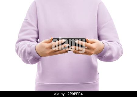 Kurze Aufnahme einer Frau in einem lavendelfarbenen Pullover, die das Smartphone mit beiden Händen horizontal hält. Stockfoto