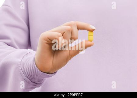 Gekürzte Aufnahme einer Frau in einem übergroßen, lavendelfarbenen Sweatshirt mit einer gelben Pille. Schließen. Stockfoto