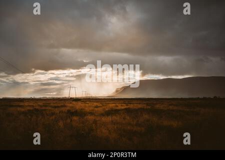 Islands wilde Schönheitssturmwolken Rollen ein, wenn das Sonnenlicht durchbricht und Schatten über das Plateau, die Berge und eine Reihe endloser Pylonen werfen Stockfoto