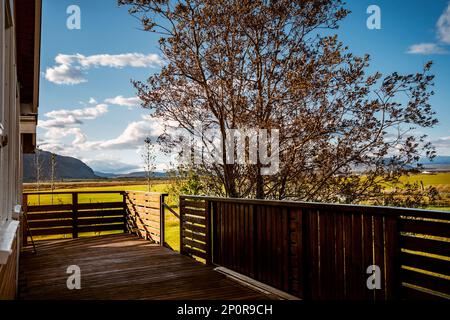 Hübsches hölzernes Chalet in Selfoss Island im Sommer mit grünem Grasland und Bergkette im Hintergrund Stockfoto