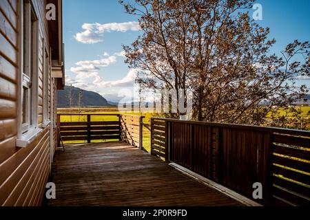 Hübsches hölzernes Chalet in Selfoss Island im Sommer mit grünem Grasland und Bergkette im Hintergrund Stockfoto