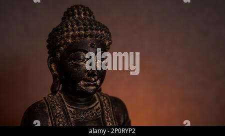 Buddha-Statue aus nächster Nähe in einer dunklen Umgebung mit goldenem Hintergrund und Kerzenlicht. Leerer Bereich für Text auf der rechten Seite Stockfoto
