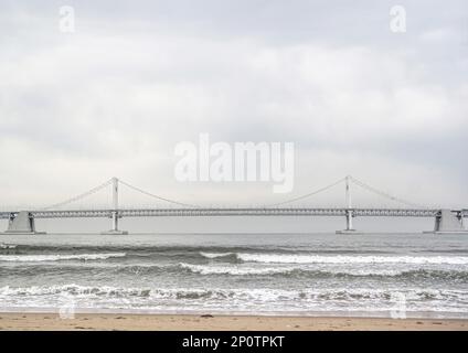 Busan, Südkorea - Mai 2019: Gwangandaegyo oder Diamond Bridge, Hängebrücke Foto vom Strand der Stadt Busan an an einem windigen Tag mit Wellen Stockfoto