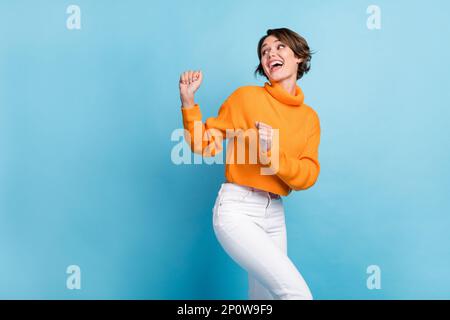 Fotoporträt einer attraktiven jungen Frau, die tanzt Look Leere Weltraumparty Tragen Sie trendige orangefarbene Kleidung isoliert auf blauem Hintergrund Stockfoto