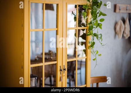 Dunkelgelbes Bücherregal aus Holz an grauer Betonwand. Um grüne Töpfe mit Hausblumen. Skandinavisches Apartment im Loftstil, rustikales Design. Makrame Stockfoto